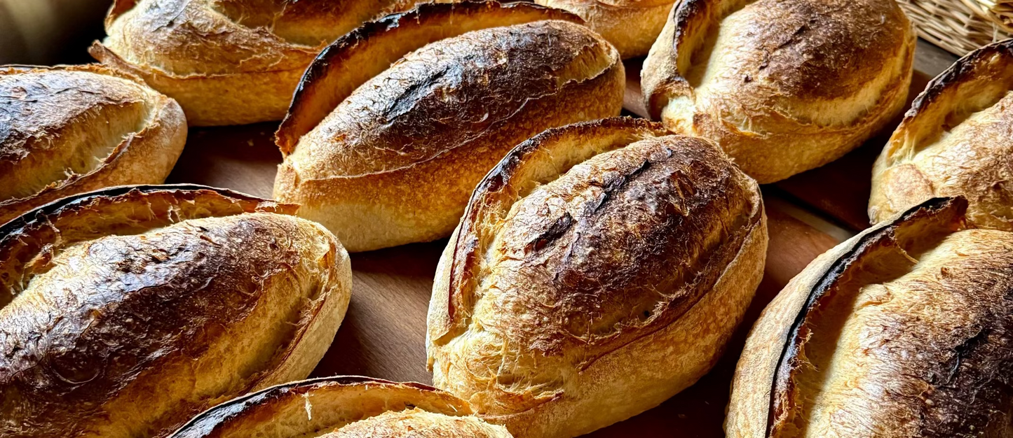 Close-up of several freshly baked sourdough bread loaves with golden-brown crusts arranged on a wooden surface.